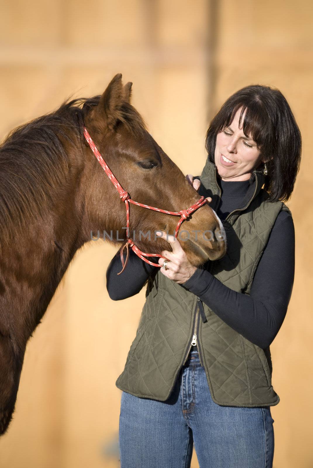Pretty dark haired woman standing with her sorrel (chestnut) quarter horse foal against an out of focus barn.