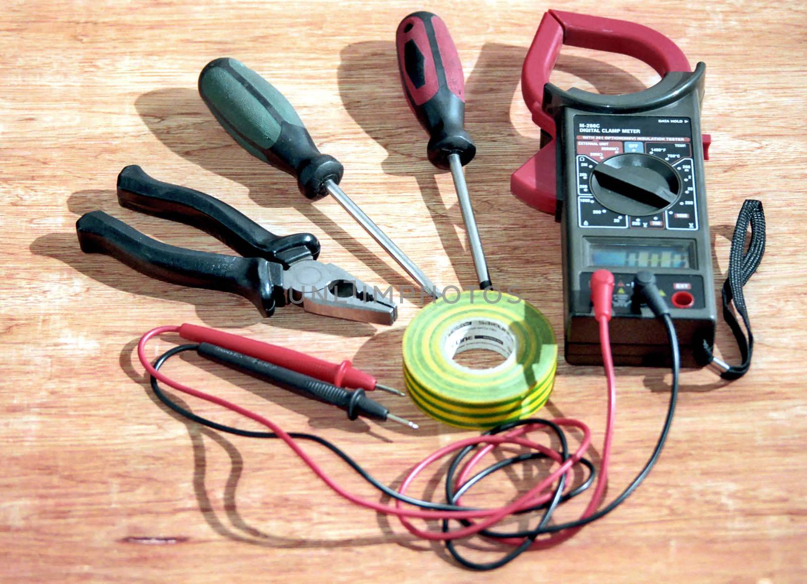 Electrician tools and digital clamp meter on wooden surface