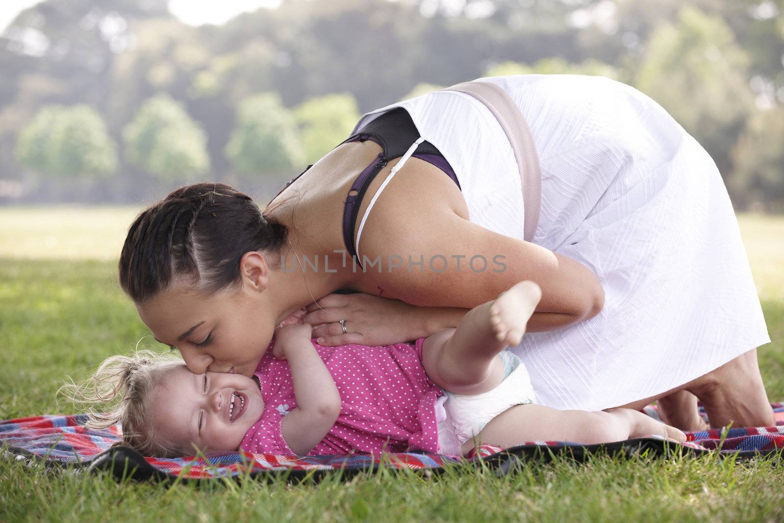 mother playing and kissing with daughter in the park in summer