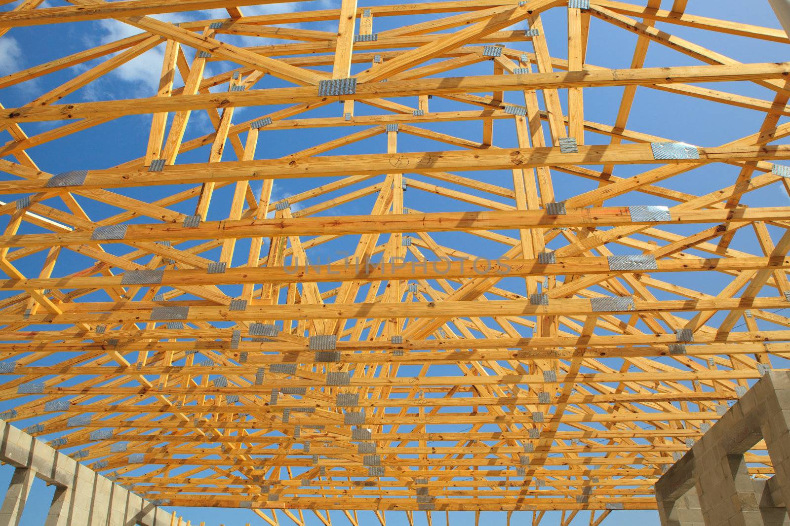Roof trusses sitting a cement block walls view from inside home. Blue sky with clouds in background
