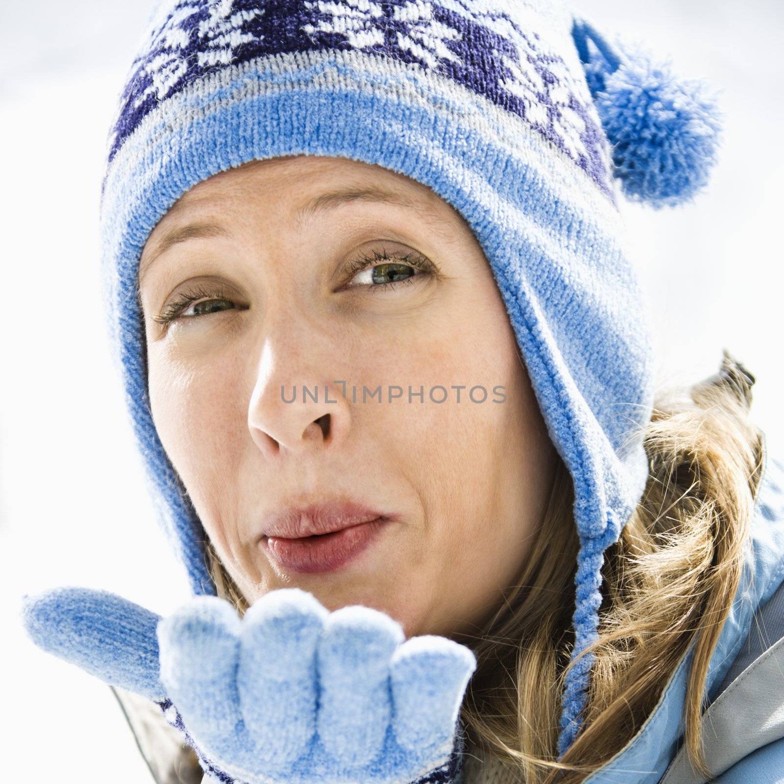 Portrait of attractive smiling mid adult Caucasian blond woman wearing blue ski cap and gloves blowing kiss at viewer.