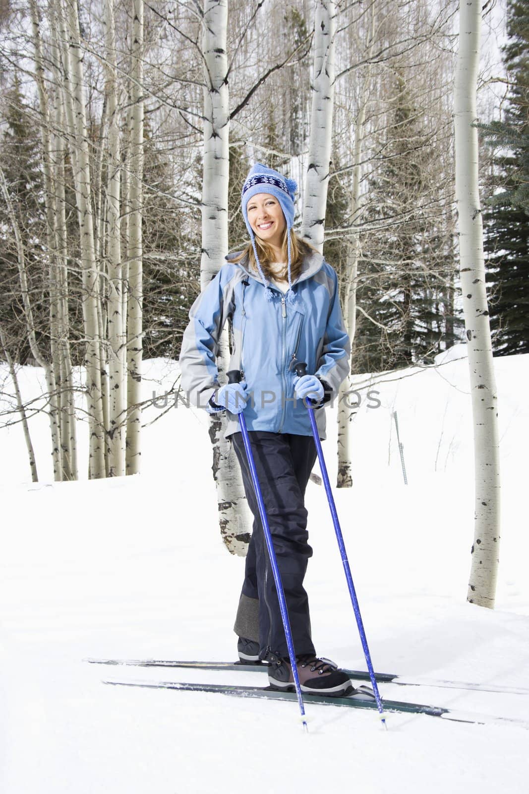 Mid adult Caucasian female skier wearing blue ski clothing standing on ski slope smiling.