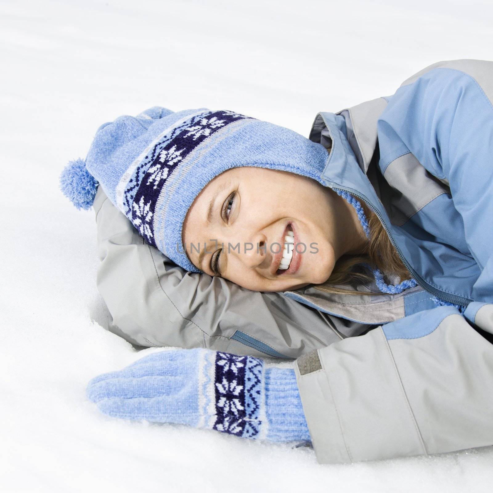 Attractive smiling mid adult Caucasian woman wearing blue ski clothing lying in snow looking at viewer.