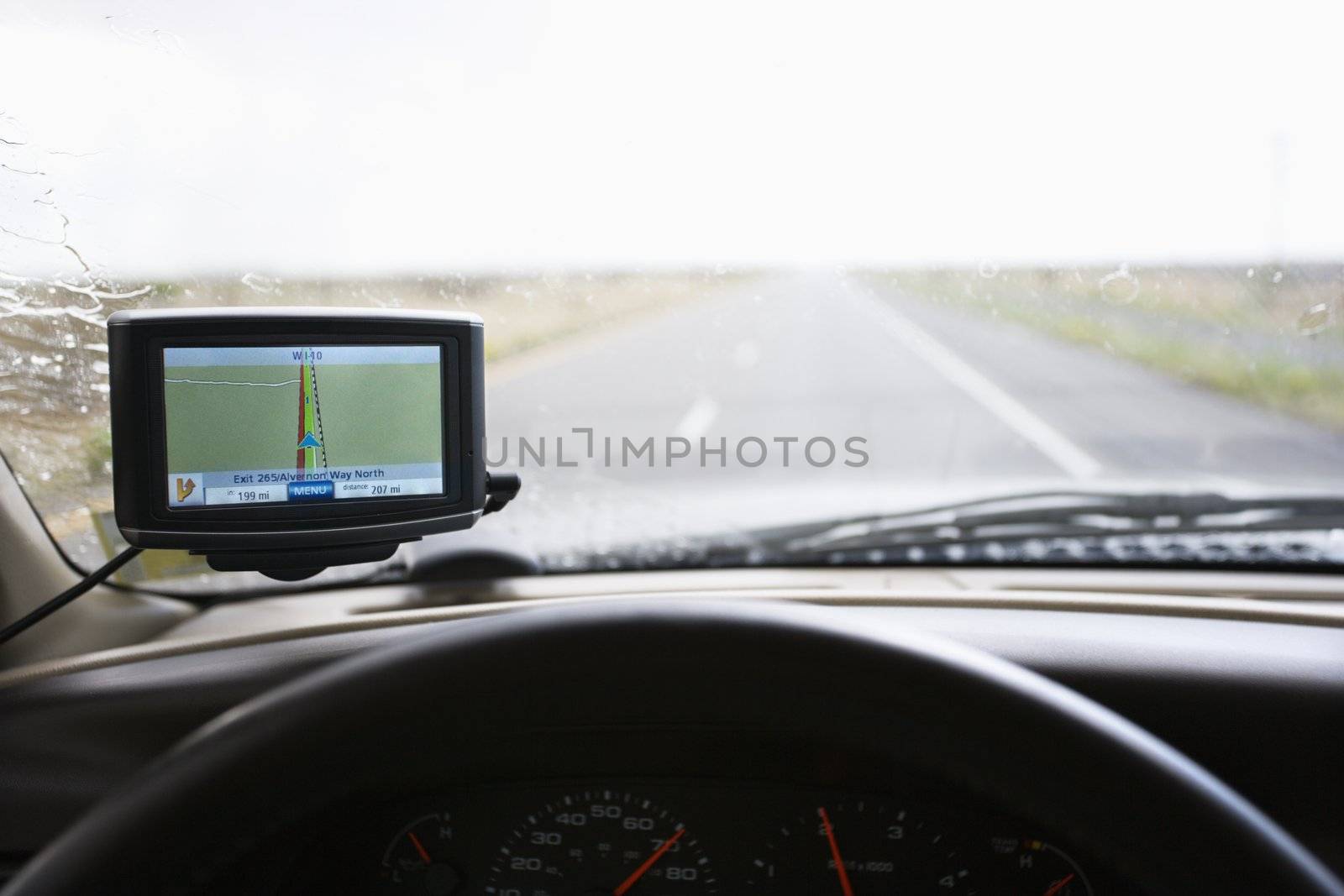 Vehicle dashboard with GPS and view through windshield of highway ahead.