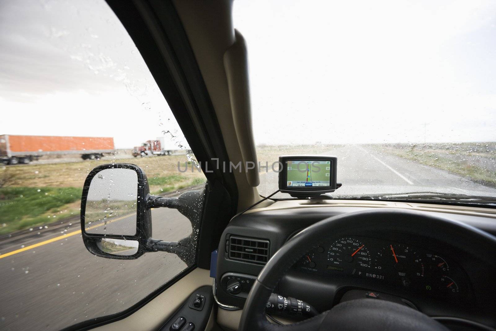 Vehicle dashboard with GPS and view through windshield of rainy highway ahead.