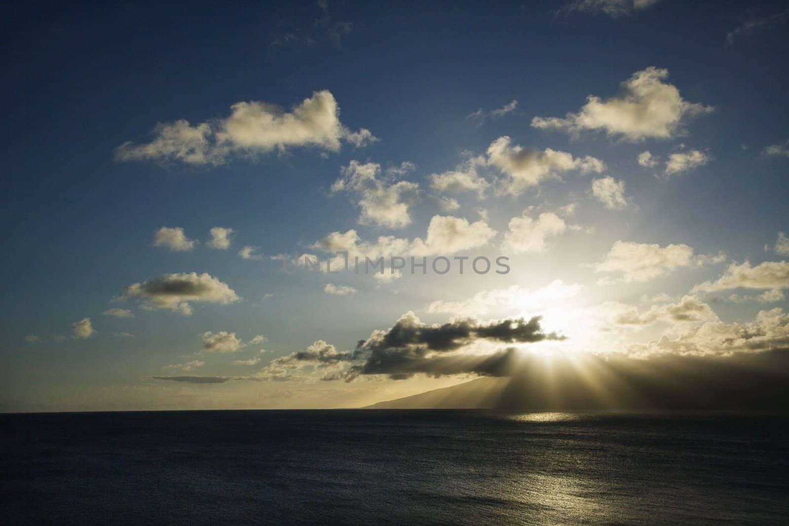 Pacific ocean and island with sun streaming through clouds.