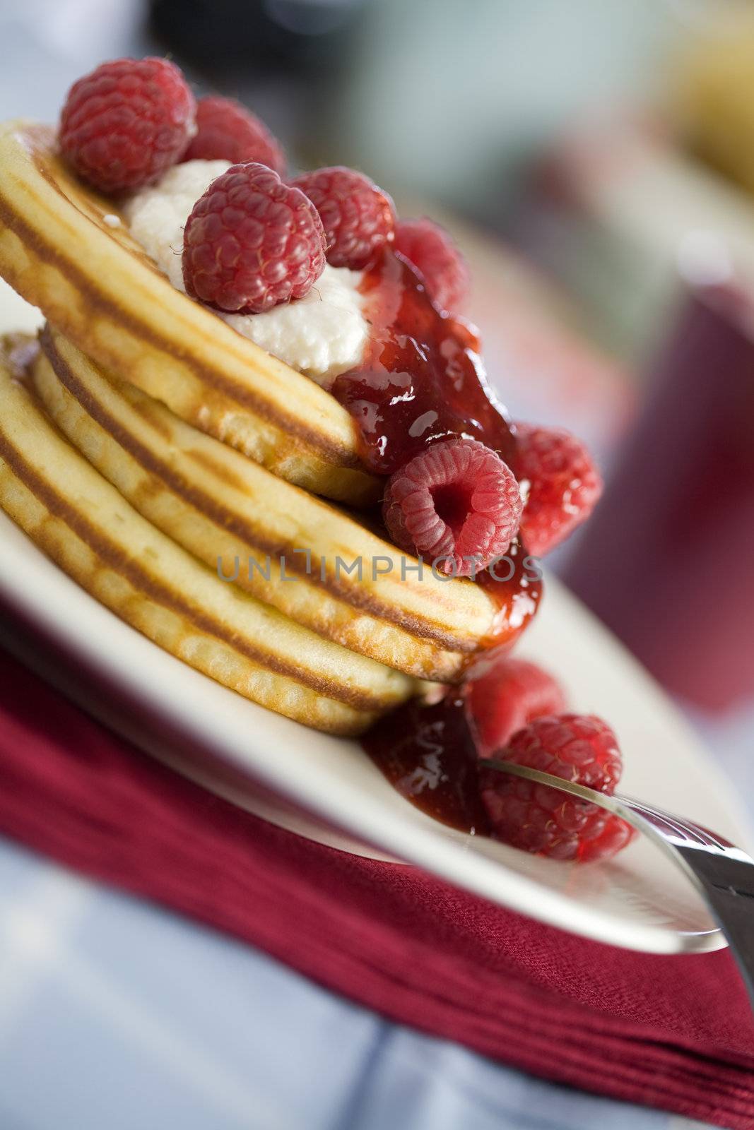 Stack of delicious american small pancakes topped with jelly and raspberries