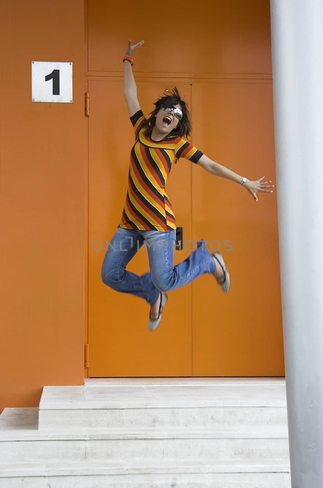 Cosmopolitan girl jumping of happiness in front of a orange building