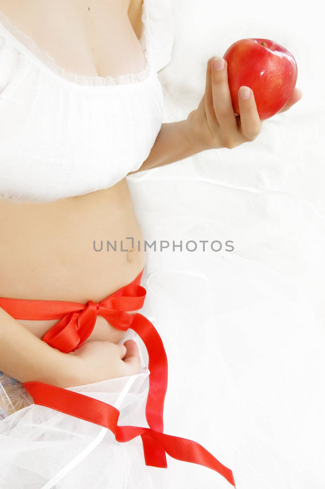 Woman hands holding pregnant belly over white with red apple and ribbon