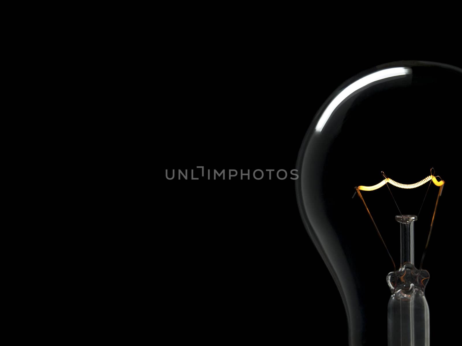 A light bulb over a black background. Tungsten glowing filament. Copy space.