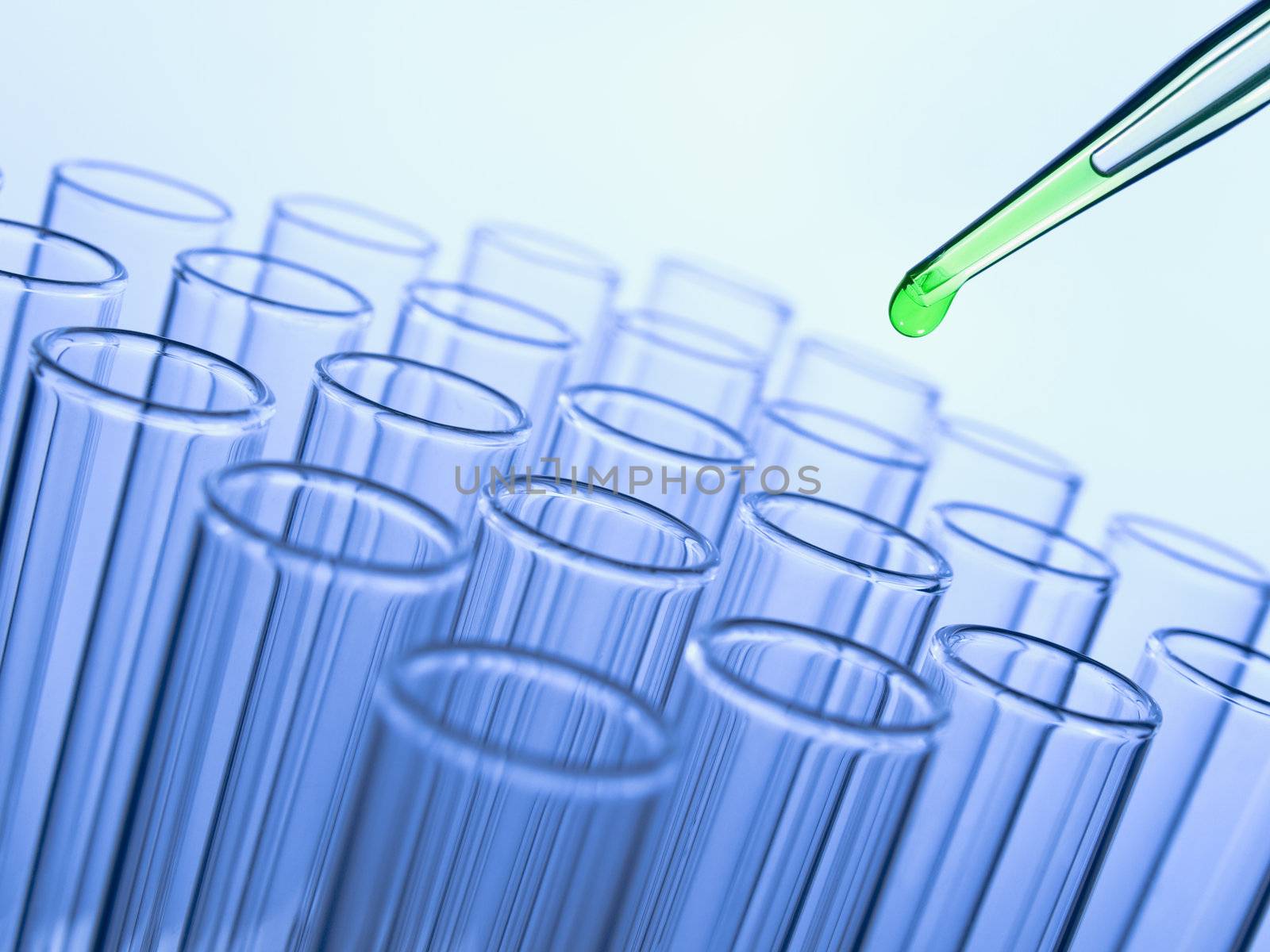 Close up of a pipette dropping a green sample into a test tube.