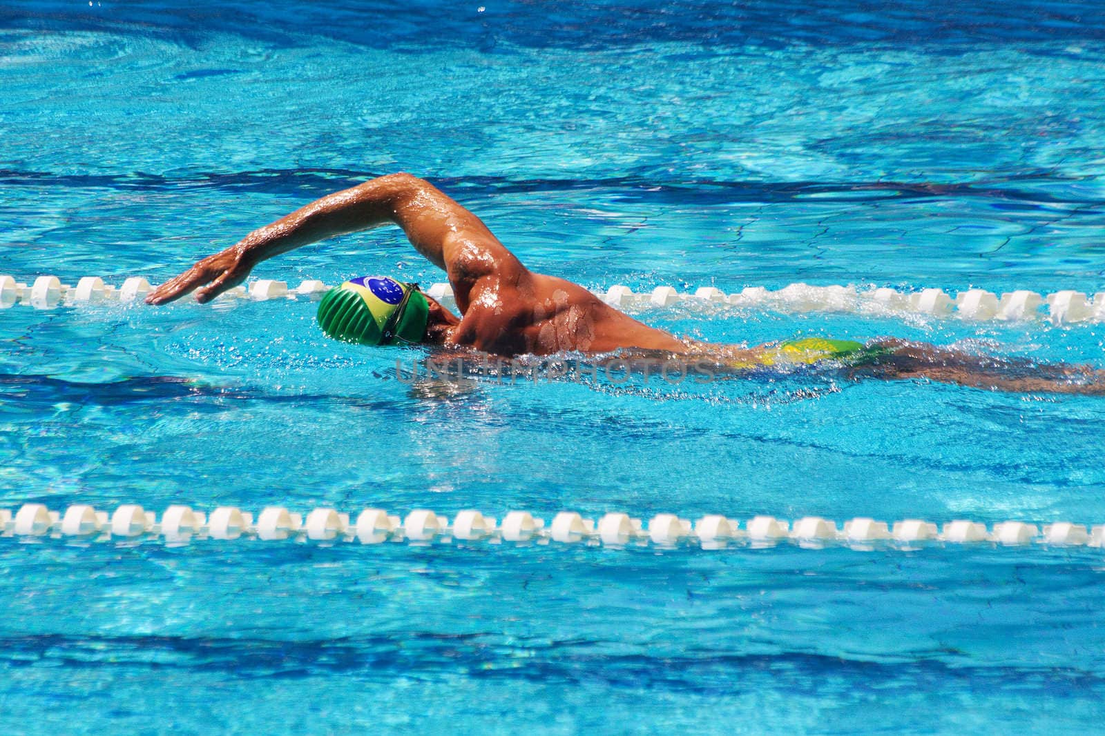 Muscular swimmer crowls in pool under bright sun