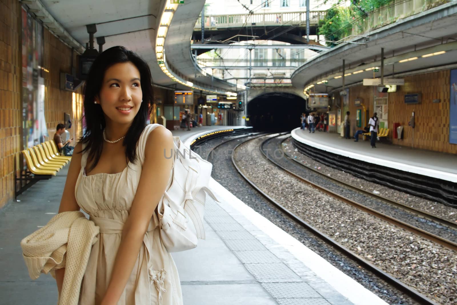 A woman waits for the train on the platform, perpective of the tracks on the right.