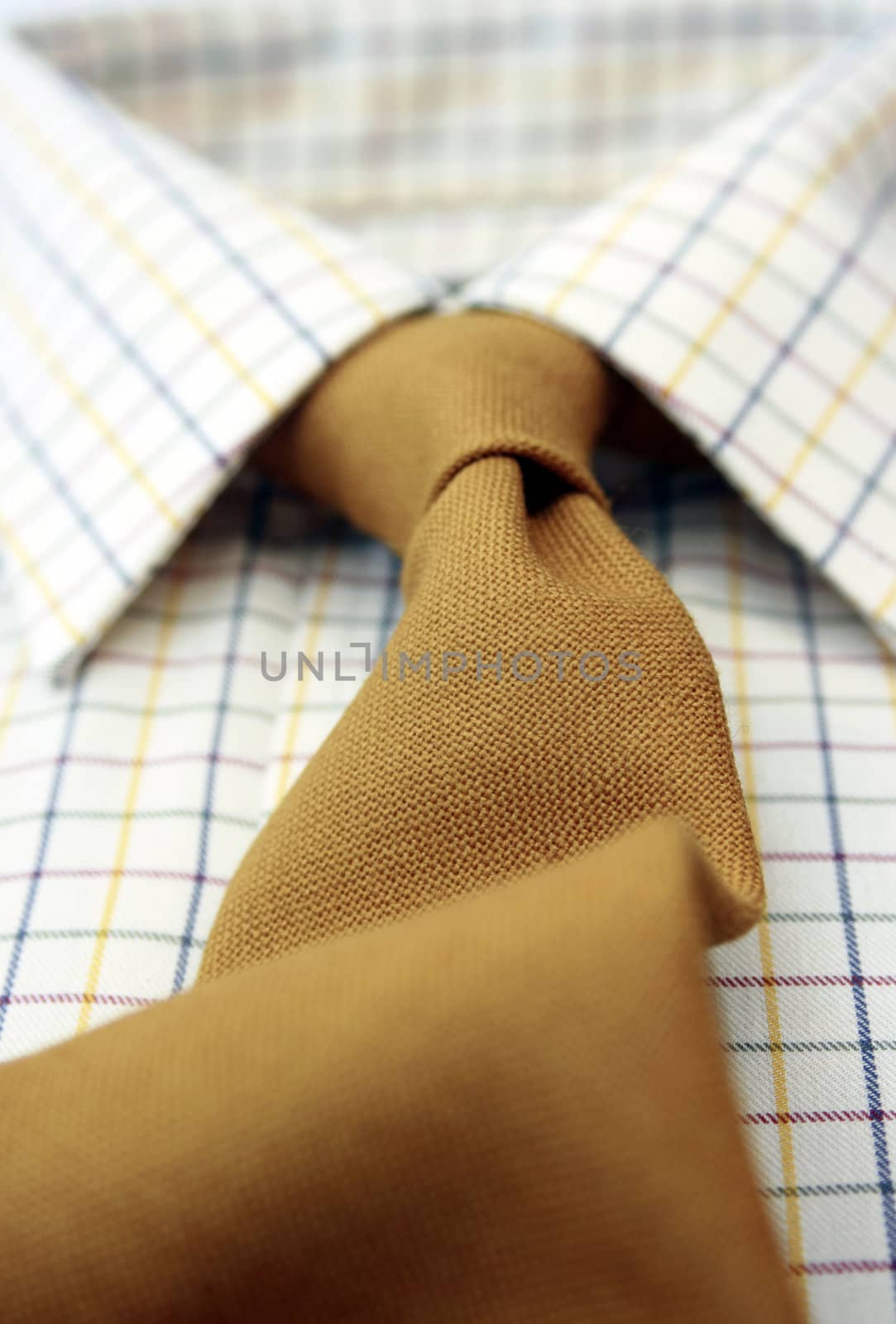 A close up view of a mans cotton checked shirt with a matching mustard colored woolen tie. Low angled view with focus to middle.