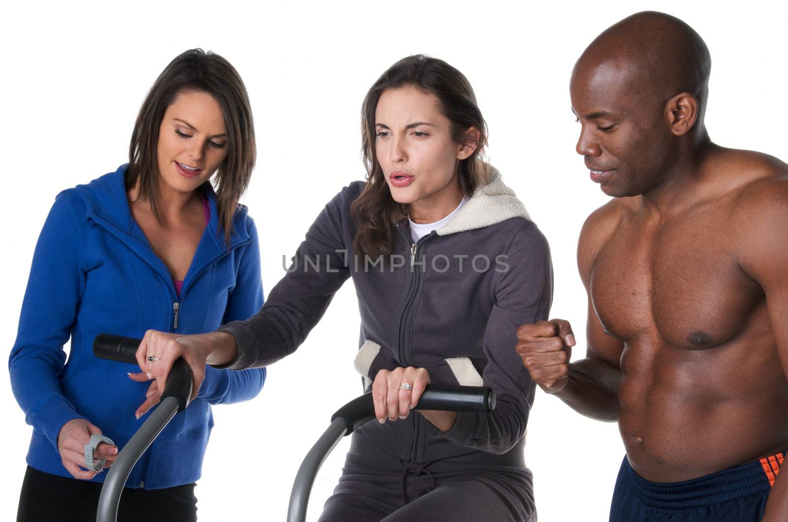 Young caucasian woman exercising in bycile while trainer encourage her and friend measure time.