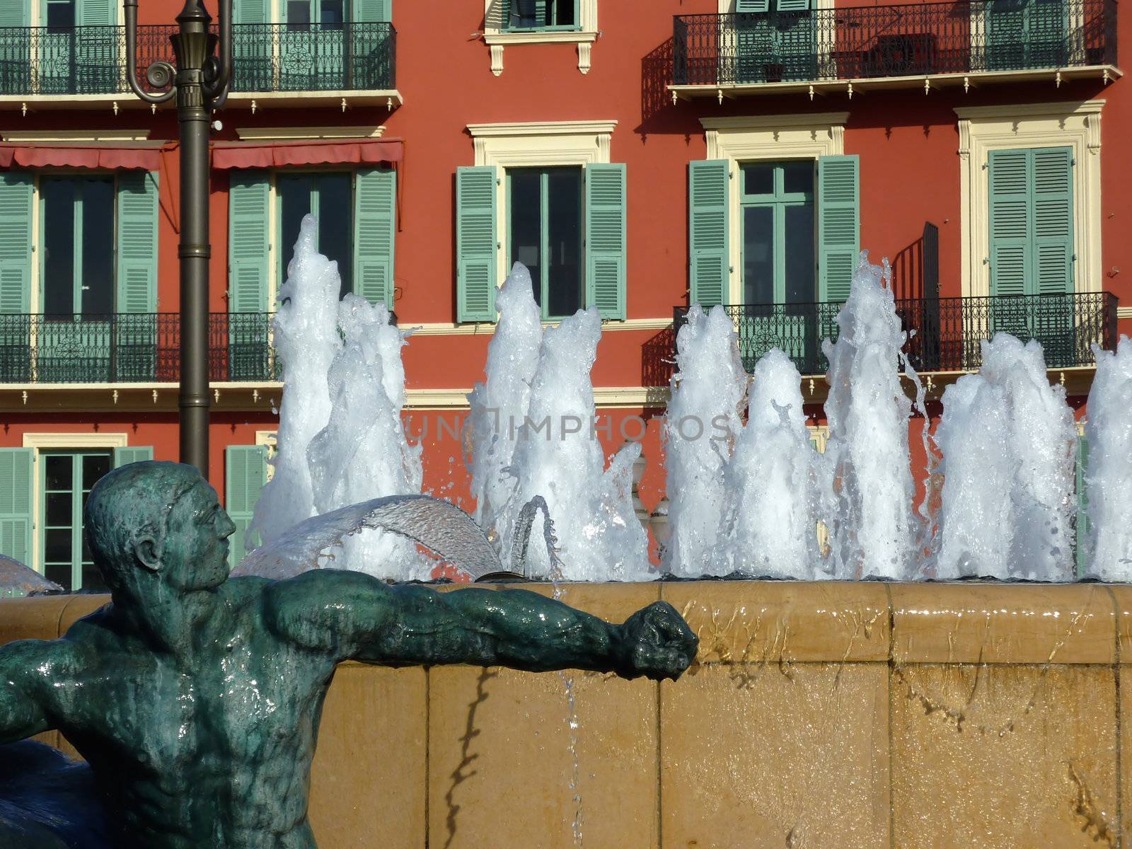 Close up of a fountain with sculptures and colored building behind it at the Massena place, Nice, France