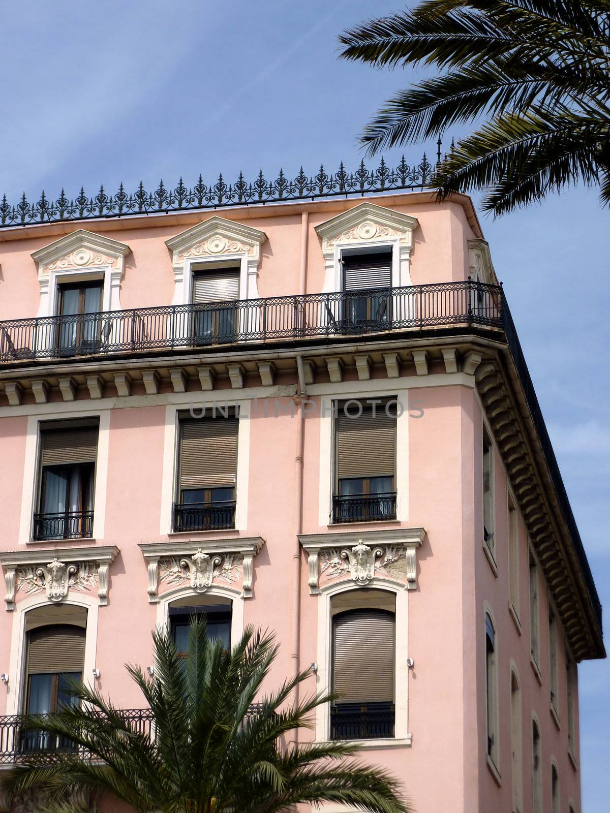 Pink old building at Nice, France, and leaves of two pal trees by beautiful weather