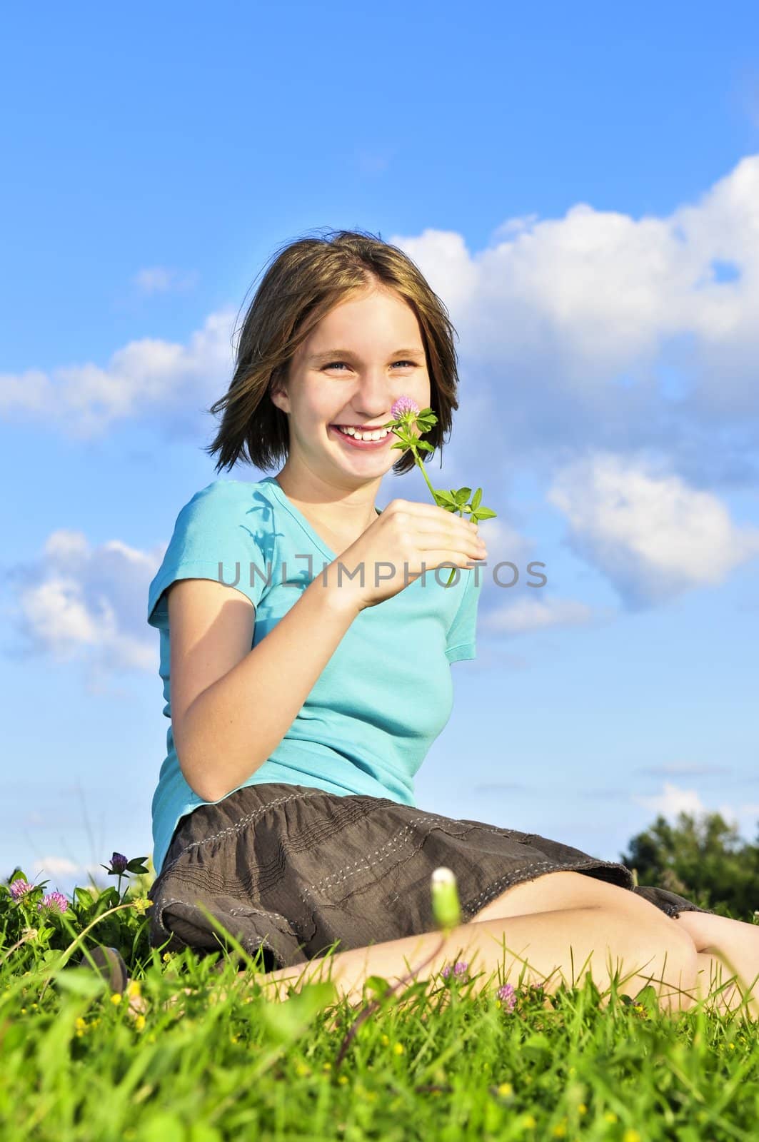 Young teenage girl sitting on grass and smelling a flower