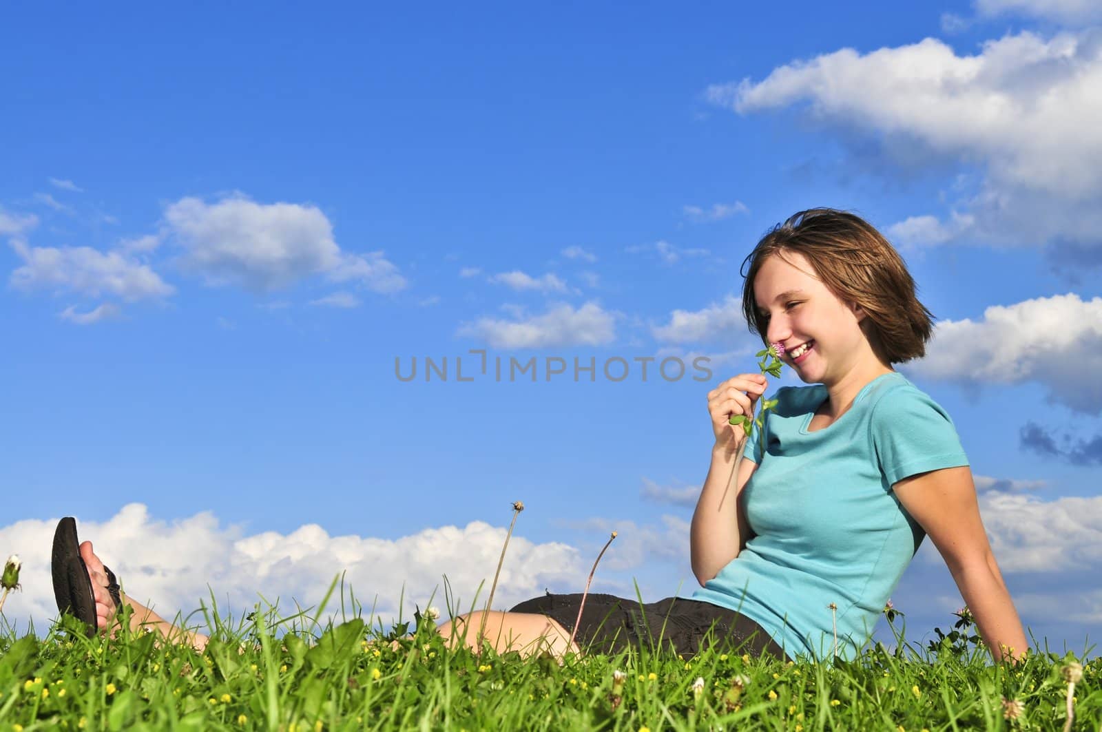 Young teenage girl sitting on grass and smelling a flower