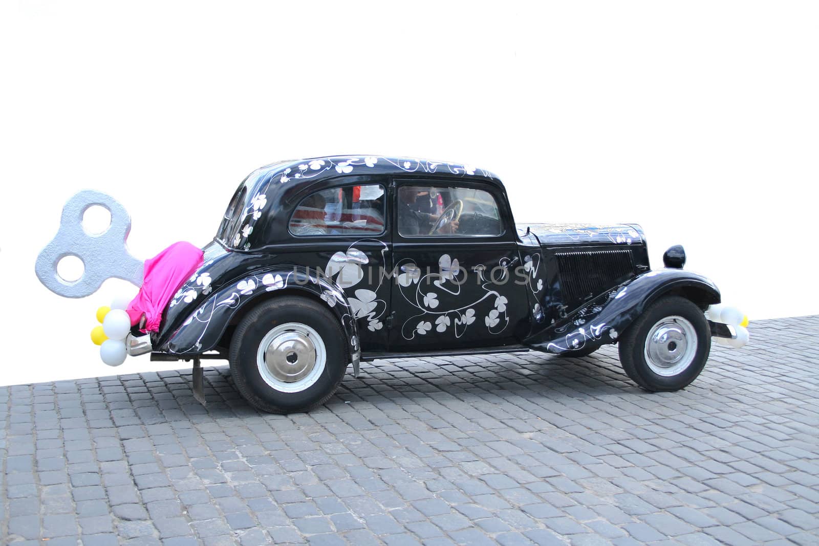The old rare automobile passing on a cobblestone road painted for a holiday