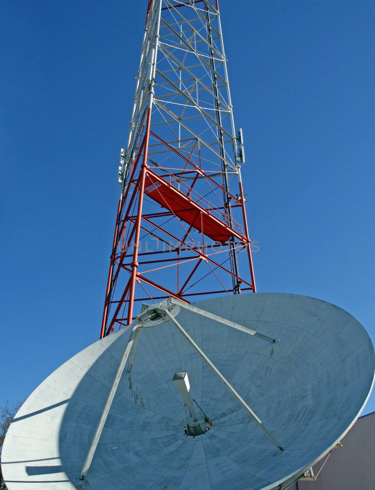 A satellite dish and radio tower on a clear blue sky.