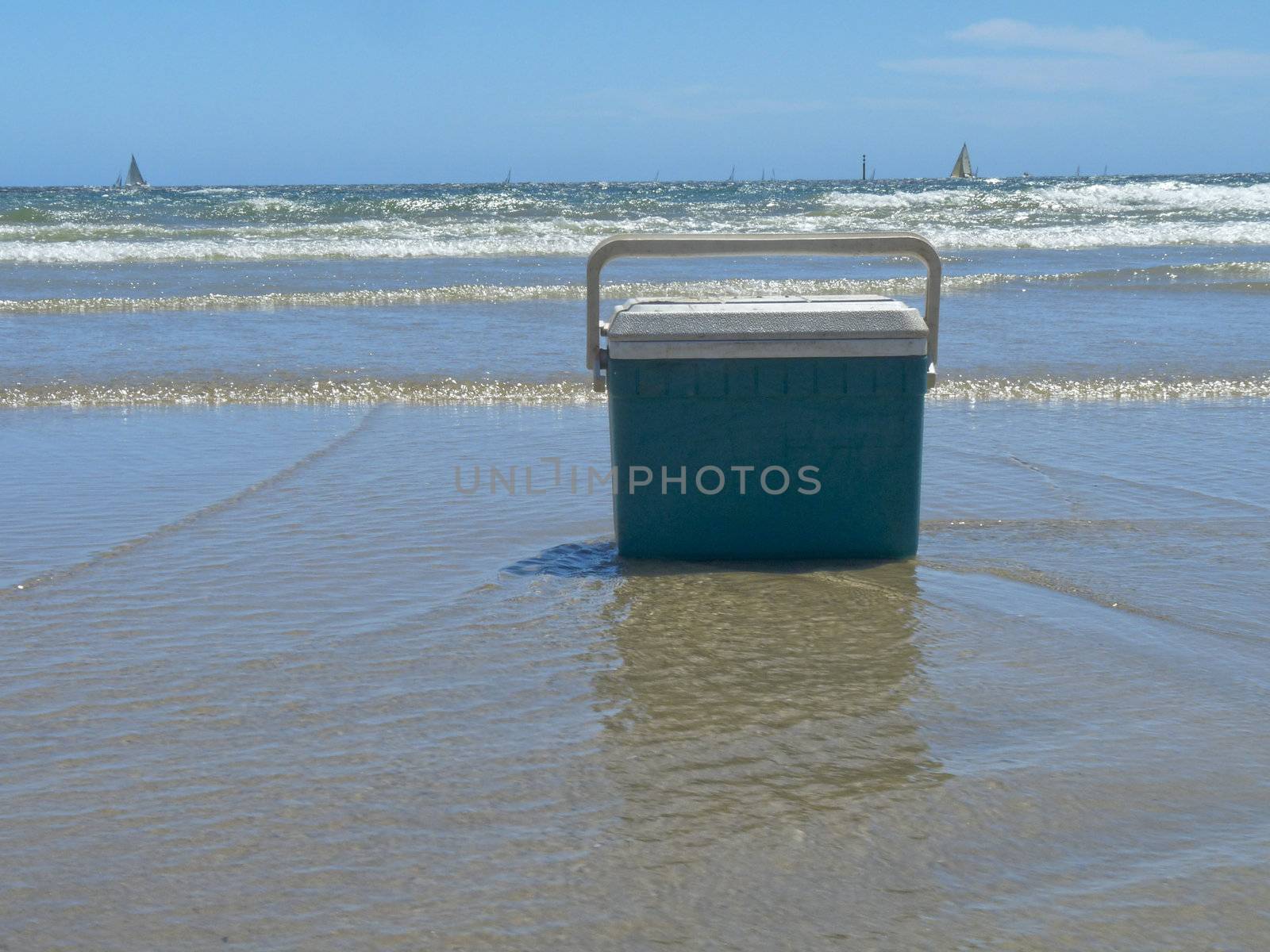 A cooler rests on the sand in the shallow water