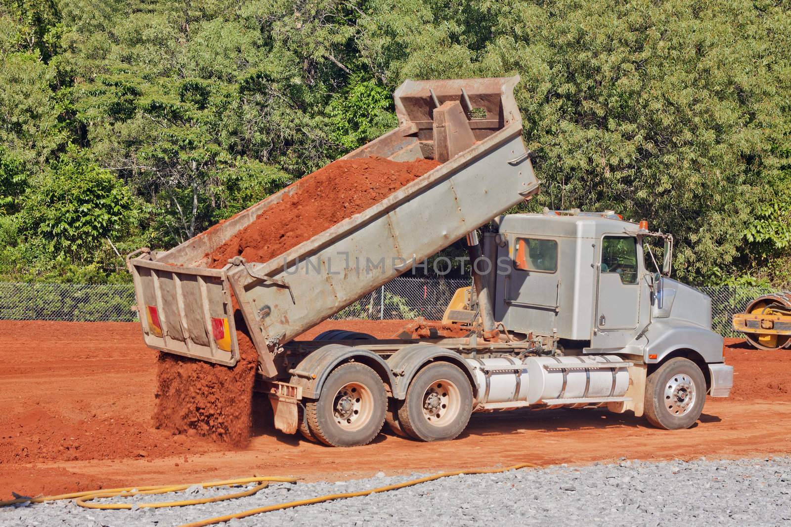 A tip truck is dumping red dirt or soil at a construction site