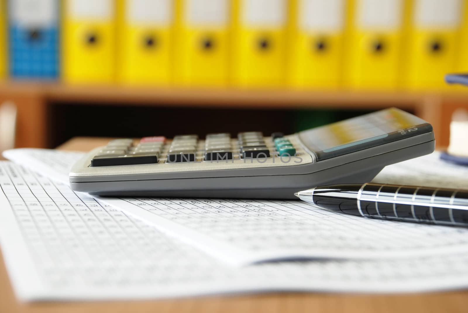 calculator on office desk side view, pen and papers