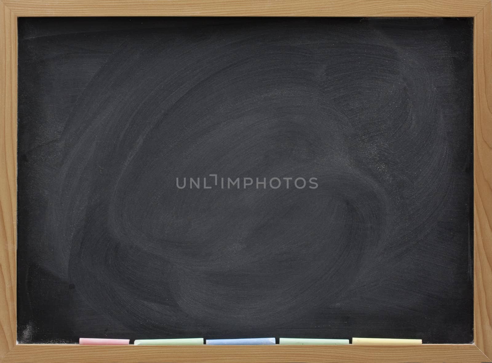 blank blackboard in wooden frame, colorful chalk sticks, and eraser smudges