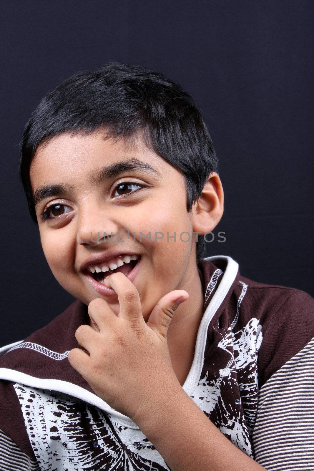 A portrait of a cute Indian boy biting his finger.