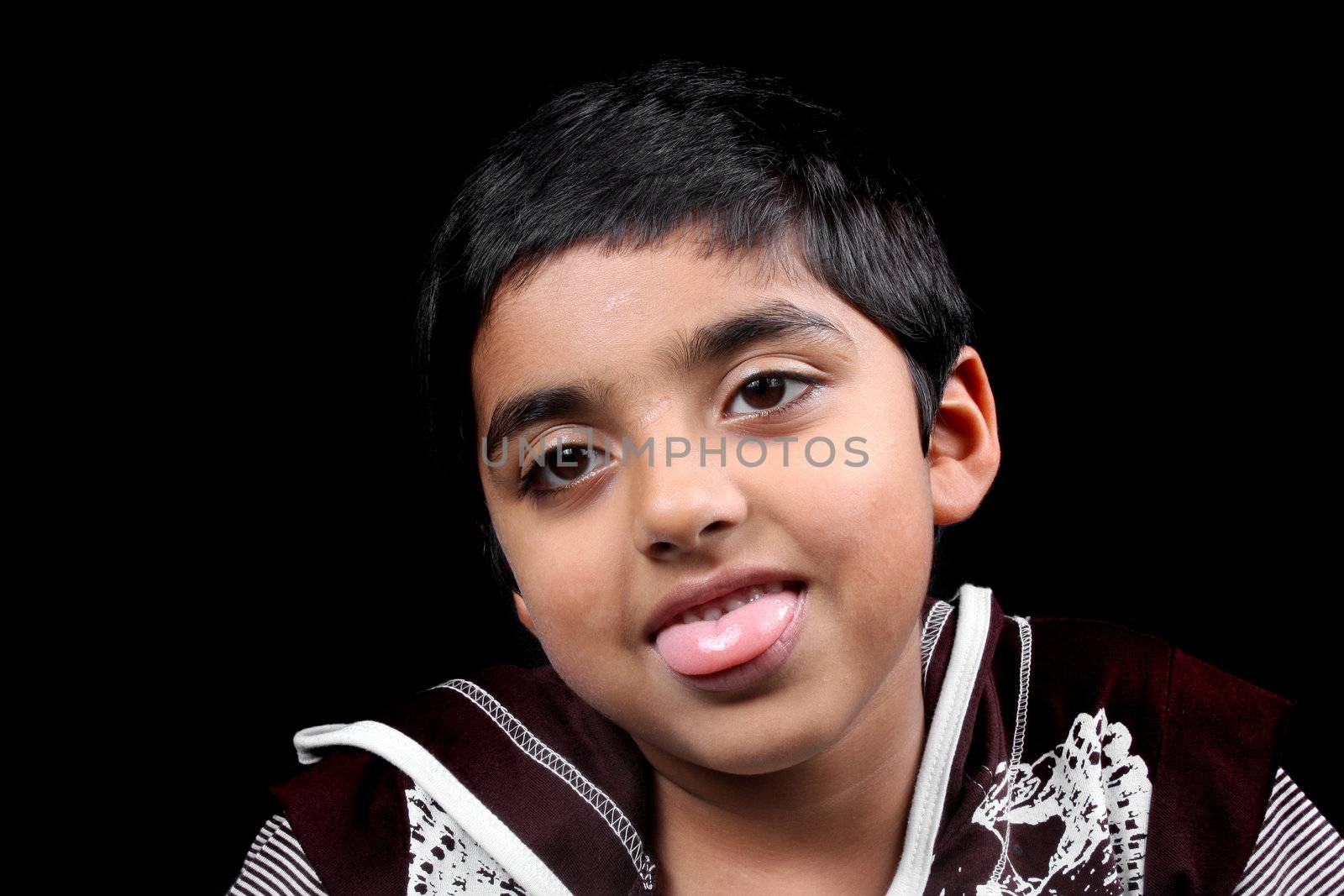 A portrait of a cute Indian boy teasing, sticking his tongue out, on black studio background.