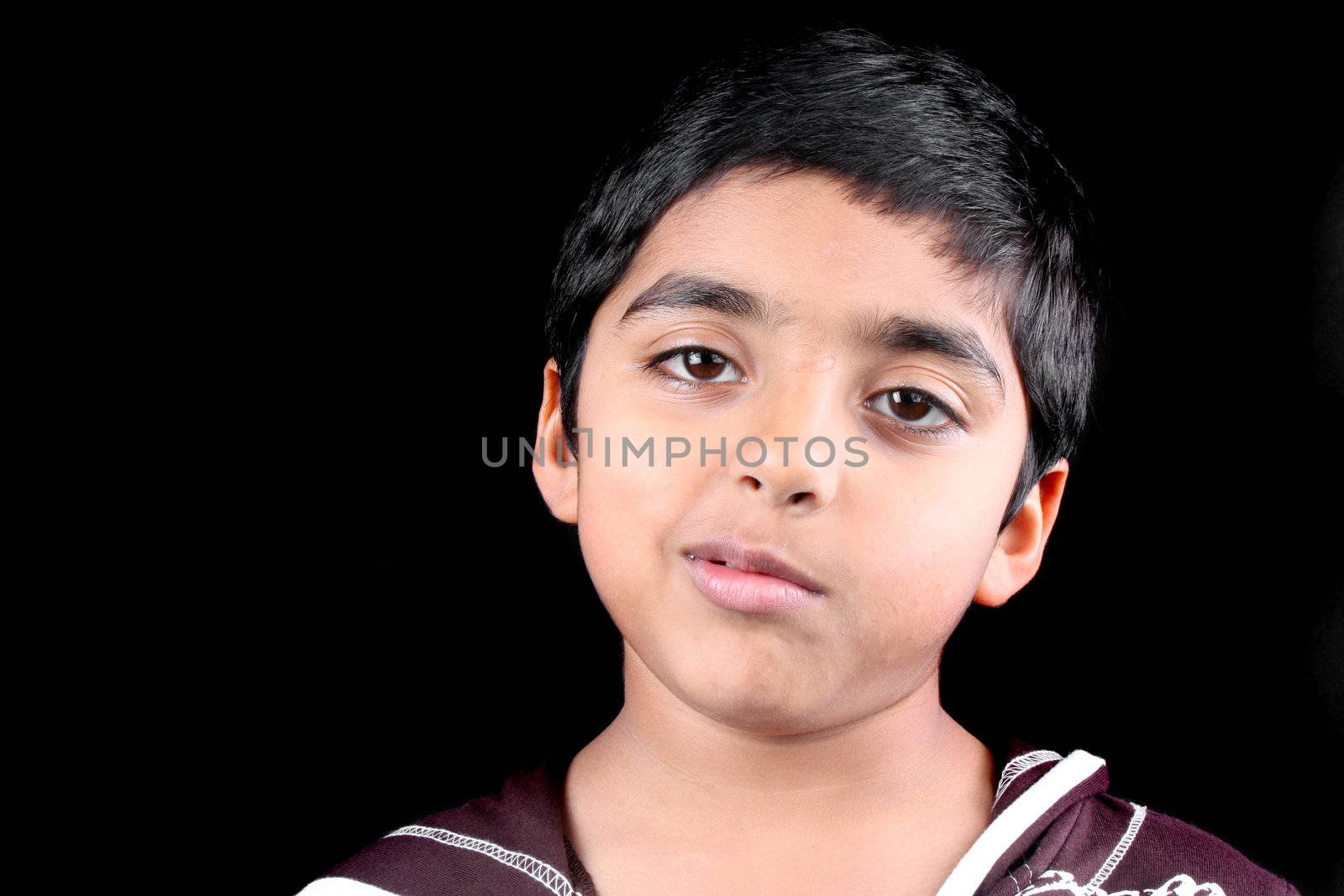 A portrait of an Indian brat with an arrogant expression on his face, on black studio background.