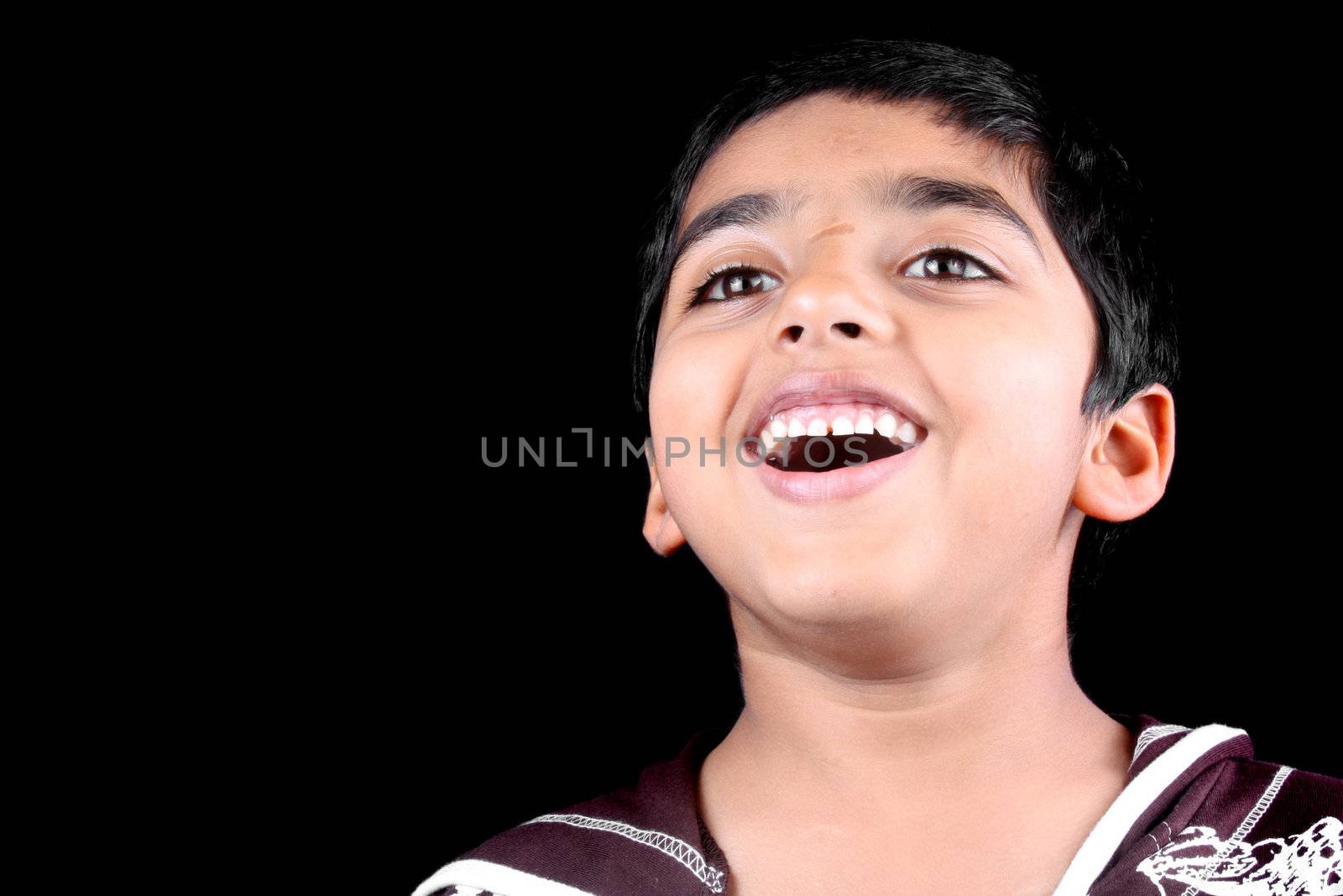A portrait of a laughing Indian kid, on black studio background.