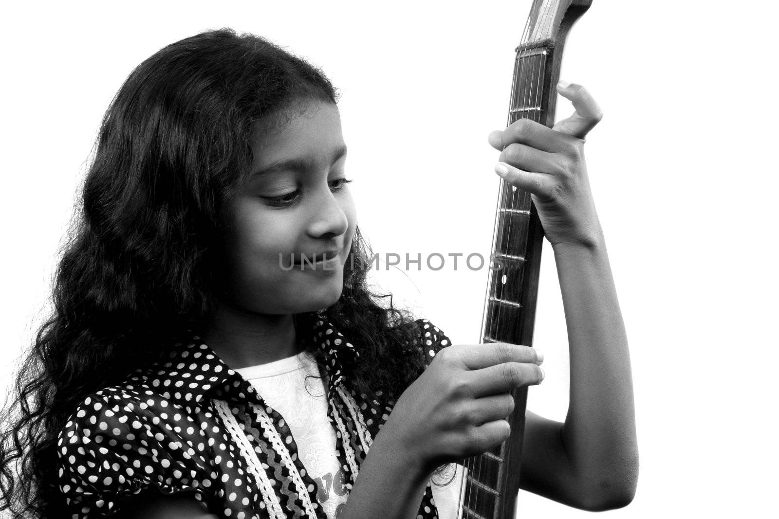 A black & white portrait of a cute Indian girl trying to study an acoustic guitar closely.