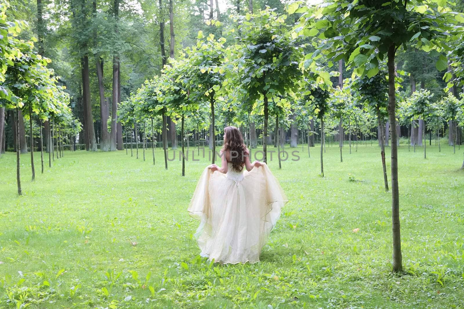 girl in white-golden gown in the summer park between young trees