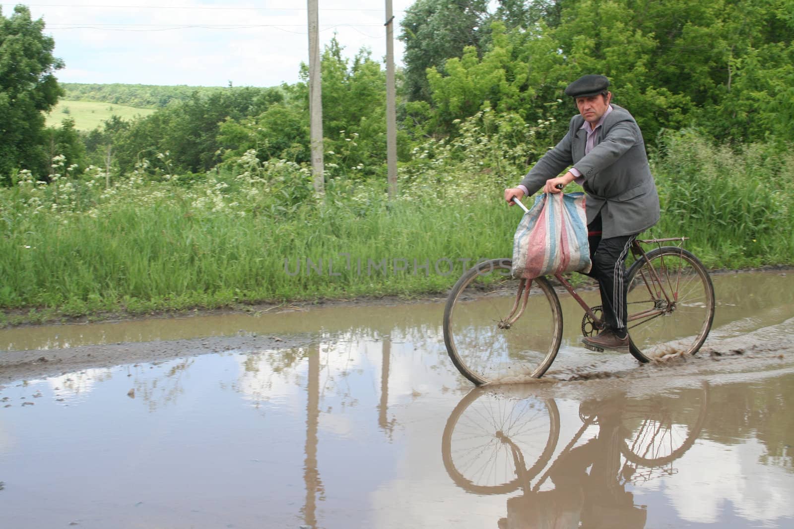 The farmer on a bicycle comes back home after work in the Kharkov area passing through rain lake 15.06.2006