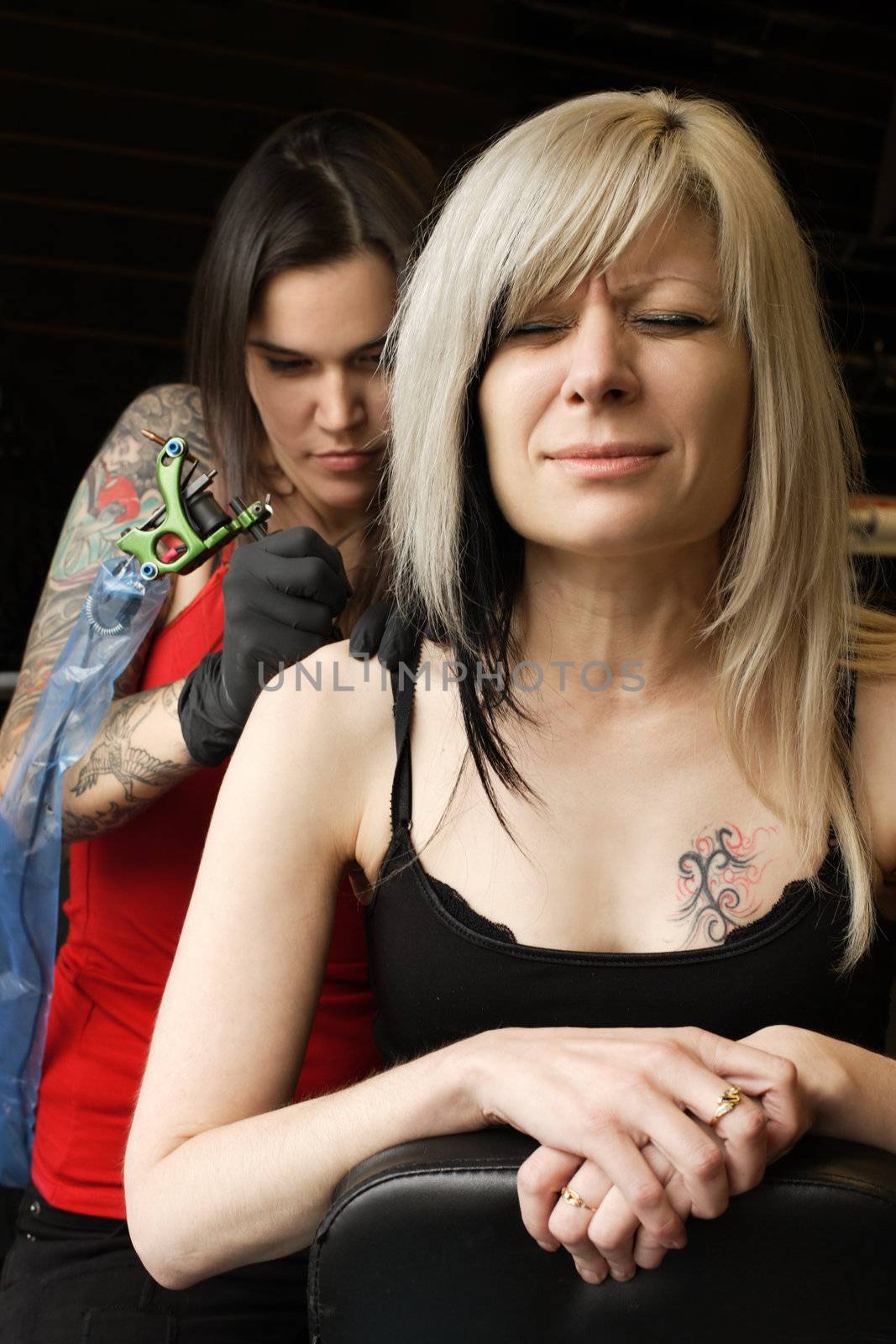 A female tattoo artist applying her craft onto the back and arm of a female in her 30's. (Property release for tattoo artwork attached)