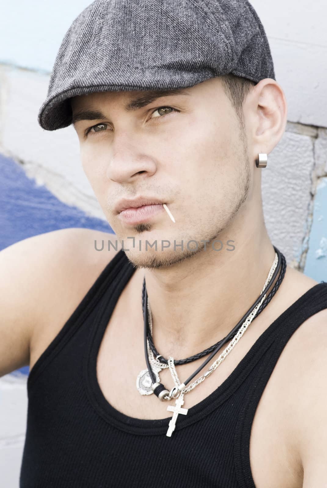 The young man is sitting on the pavement. He has blank expression on face and toothpick in mouth