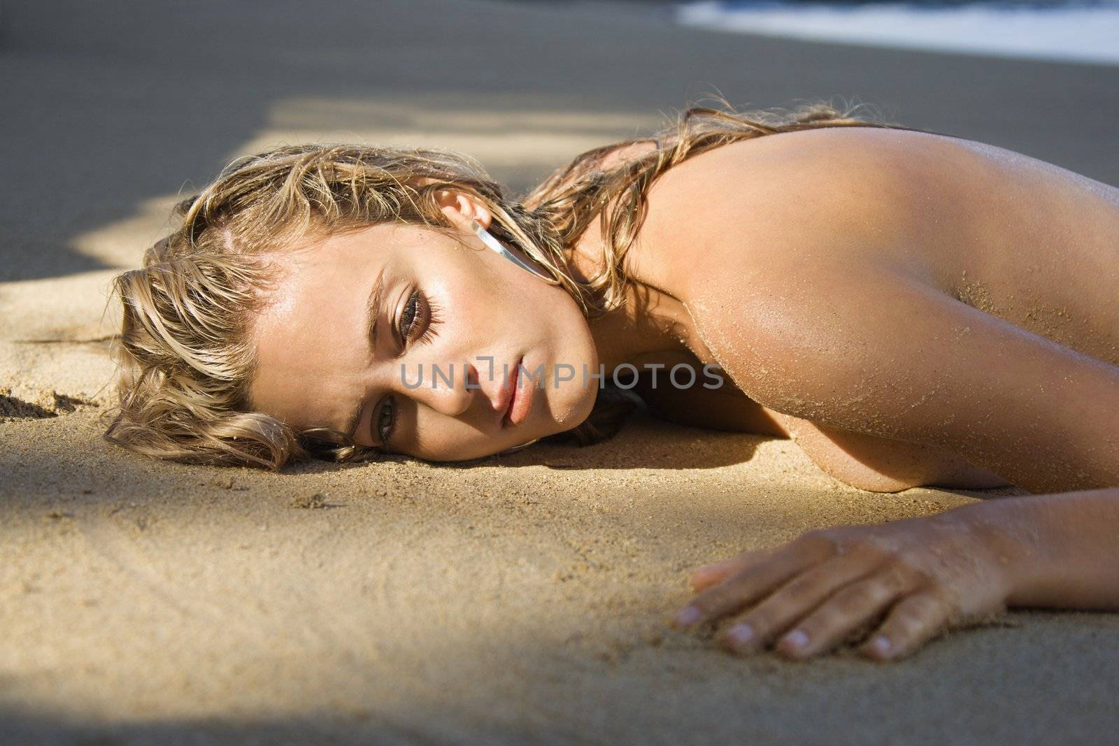Bare Caucasian blond woman lying on sand on Maui, Hawaii beach.