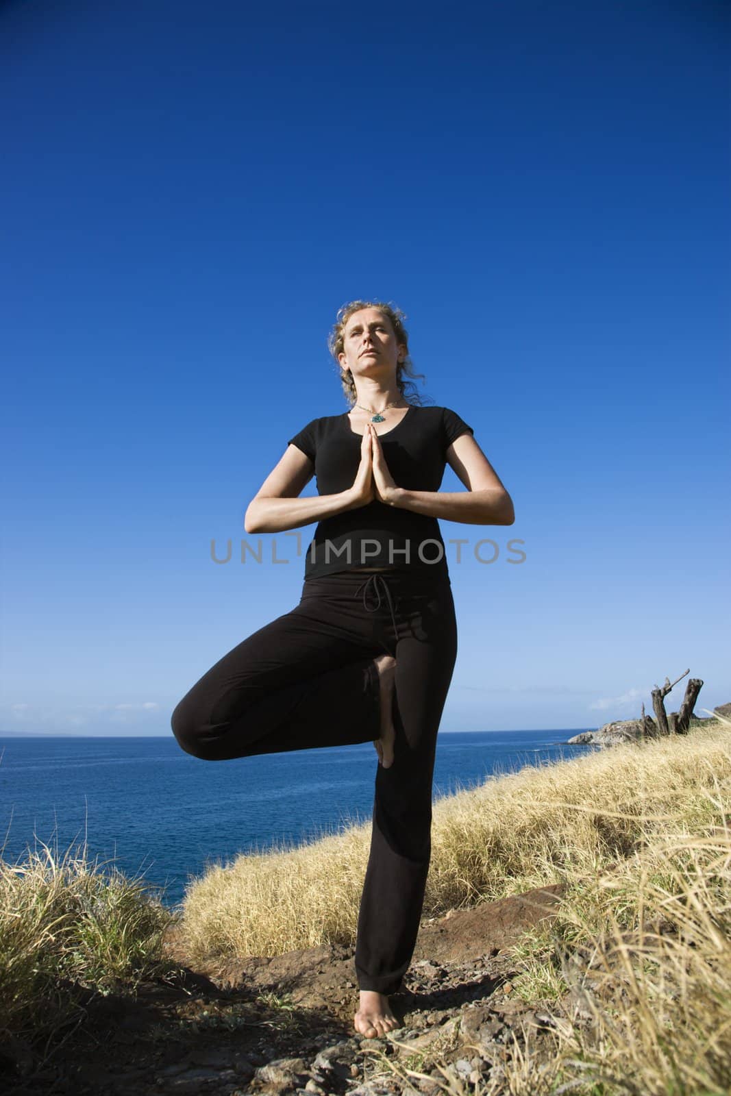 Caucasian mid-adult woman standing on Hawaiian coast in Yoga tree position.