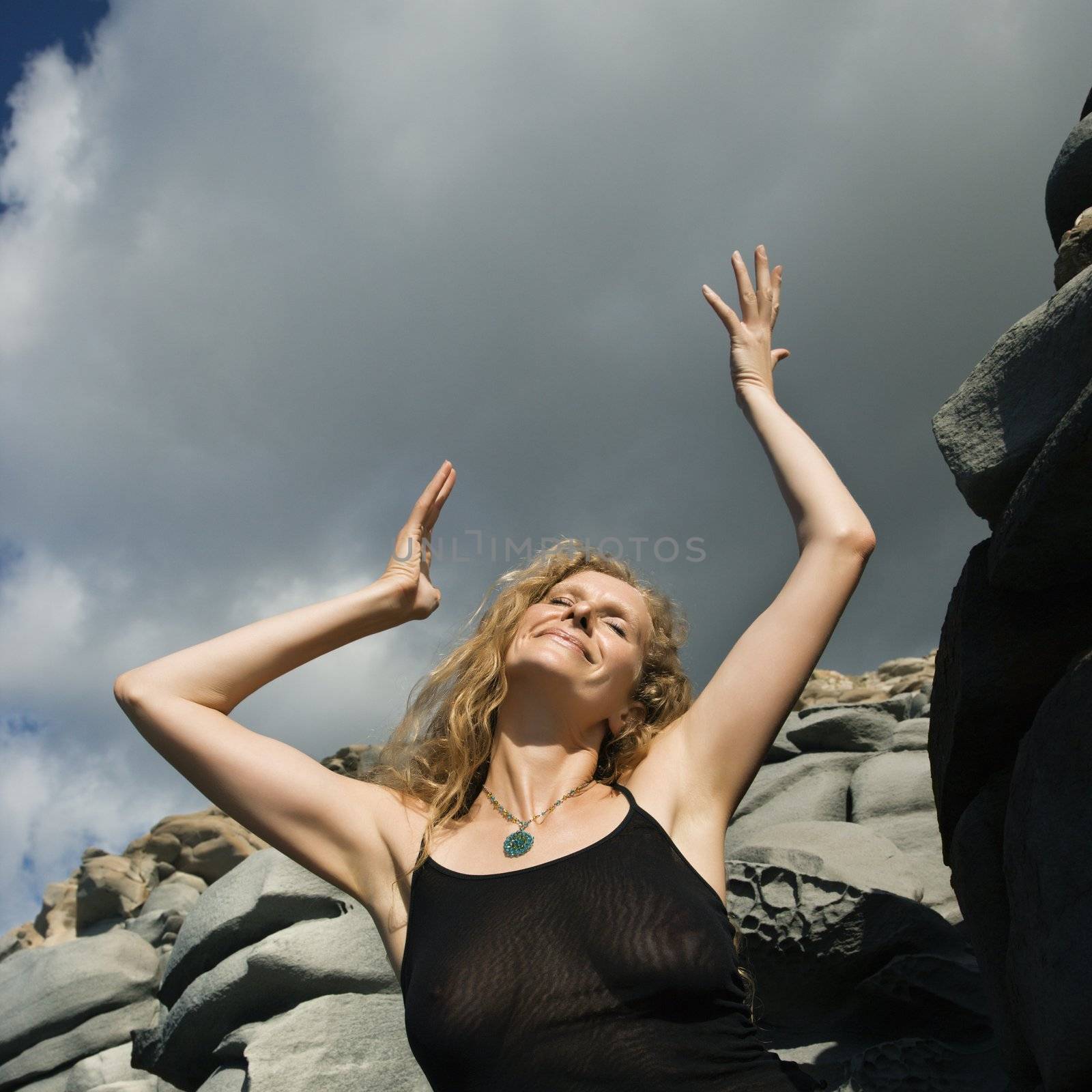 Happy Caucasian mid-adult woman with arms raised in air in rocky terrain.