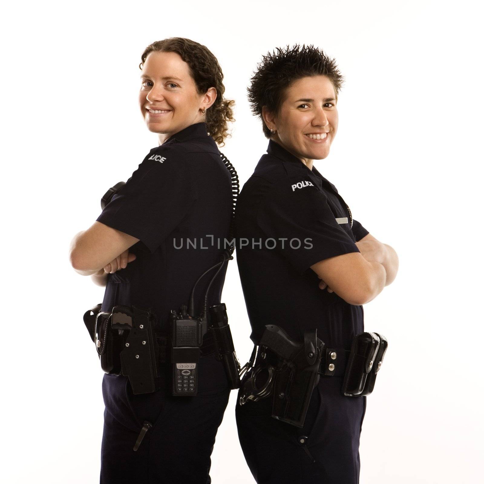 Portrait of two mid adult Caucasian policewomen standing back to back looking over their shoulders and smiling at viewer.