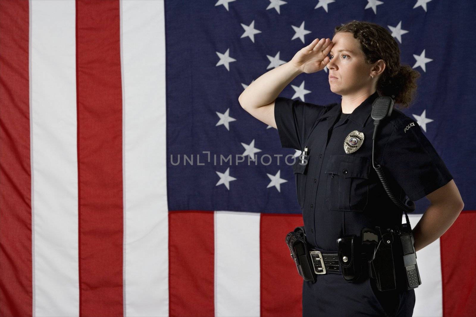 Side view of mid adult Caucasian policewoman saluting with American flag as backdrop.