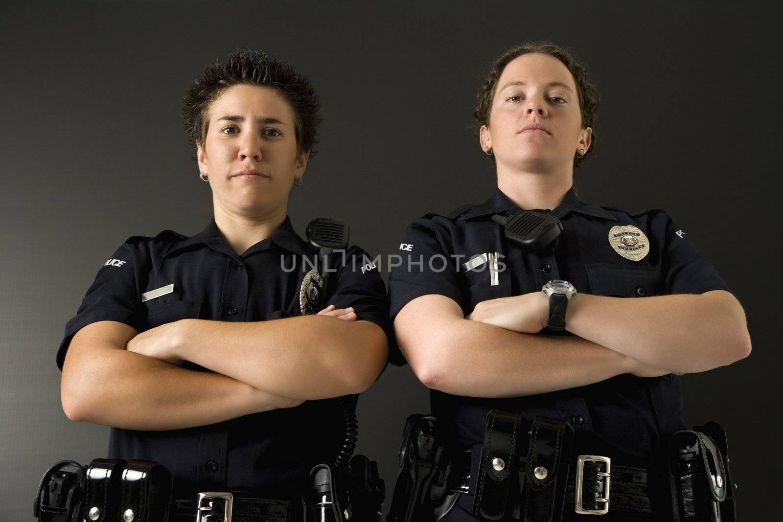 Portrait of two mid adult Caucasian policewomen standing with their arms crossed looking at viewer with serious expressions.