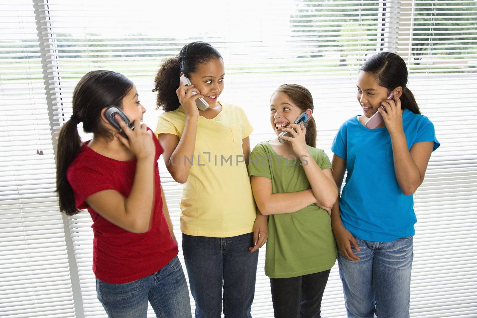 Preteen girls of mutiple ethnicities talking on cell phones.