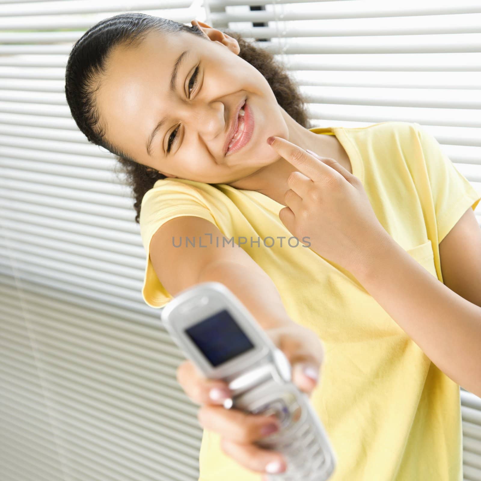 African American preteen girl holding cell phone out to viewer and smiling.