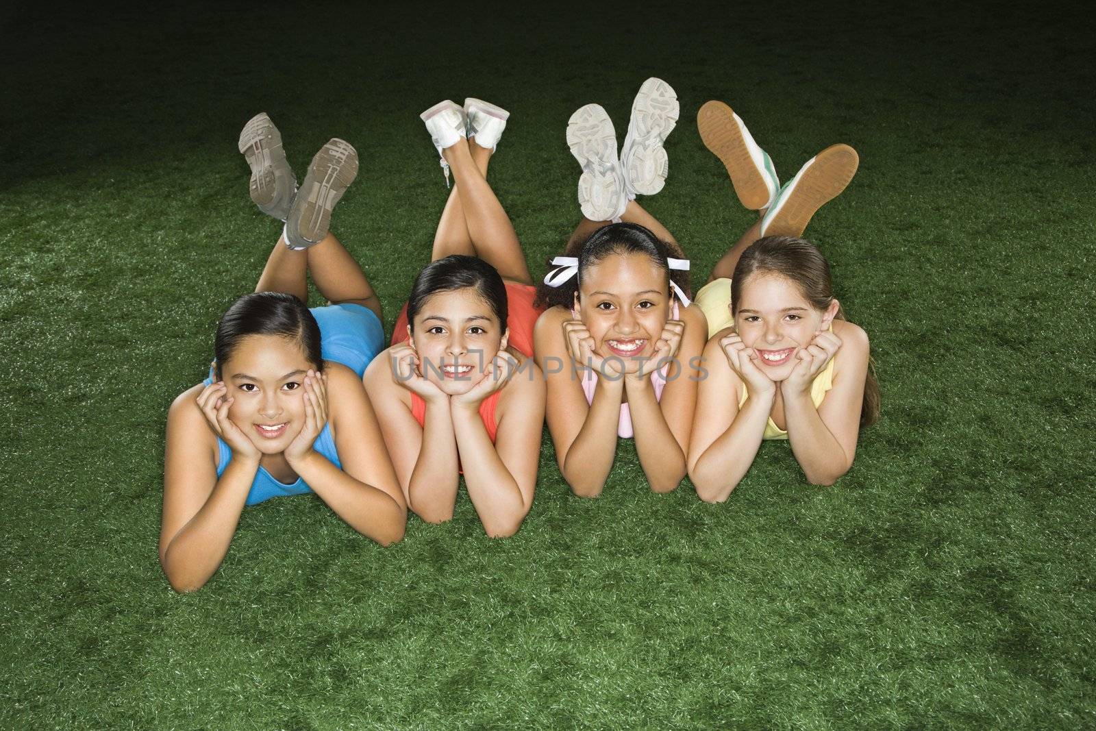 Four multiethnic girls lying on ground in indoor gym with heads on hands smiling.