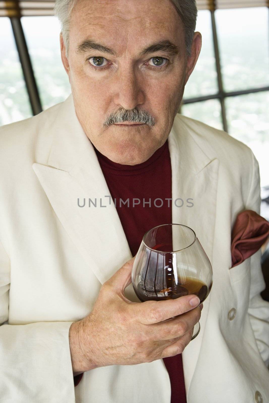 Mature Caucasian man in suit holding snifter of brandy.