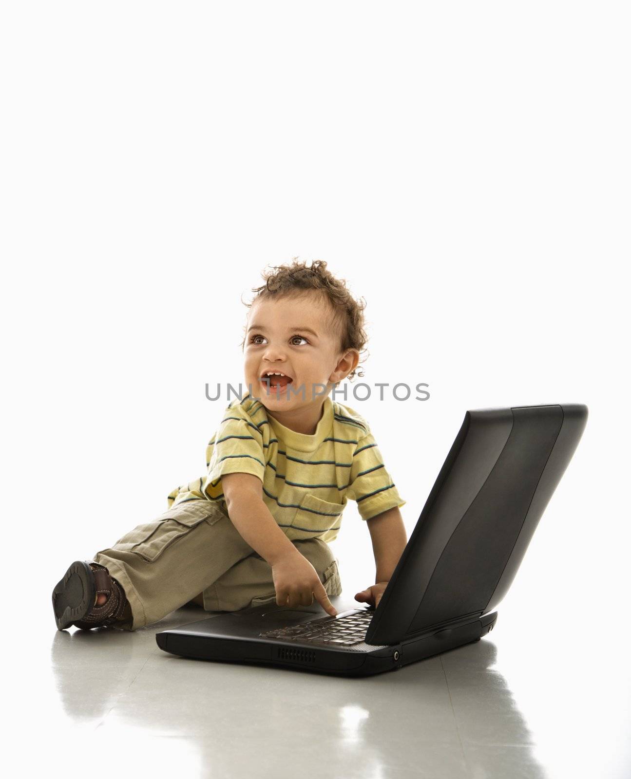 Happy African American toddler boy on laptop computer looking to side.