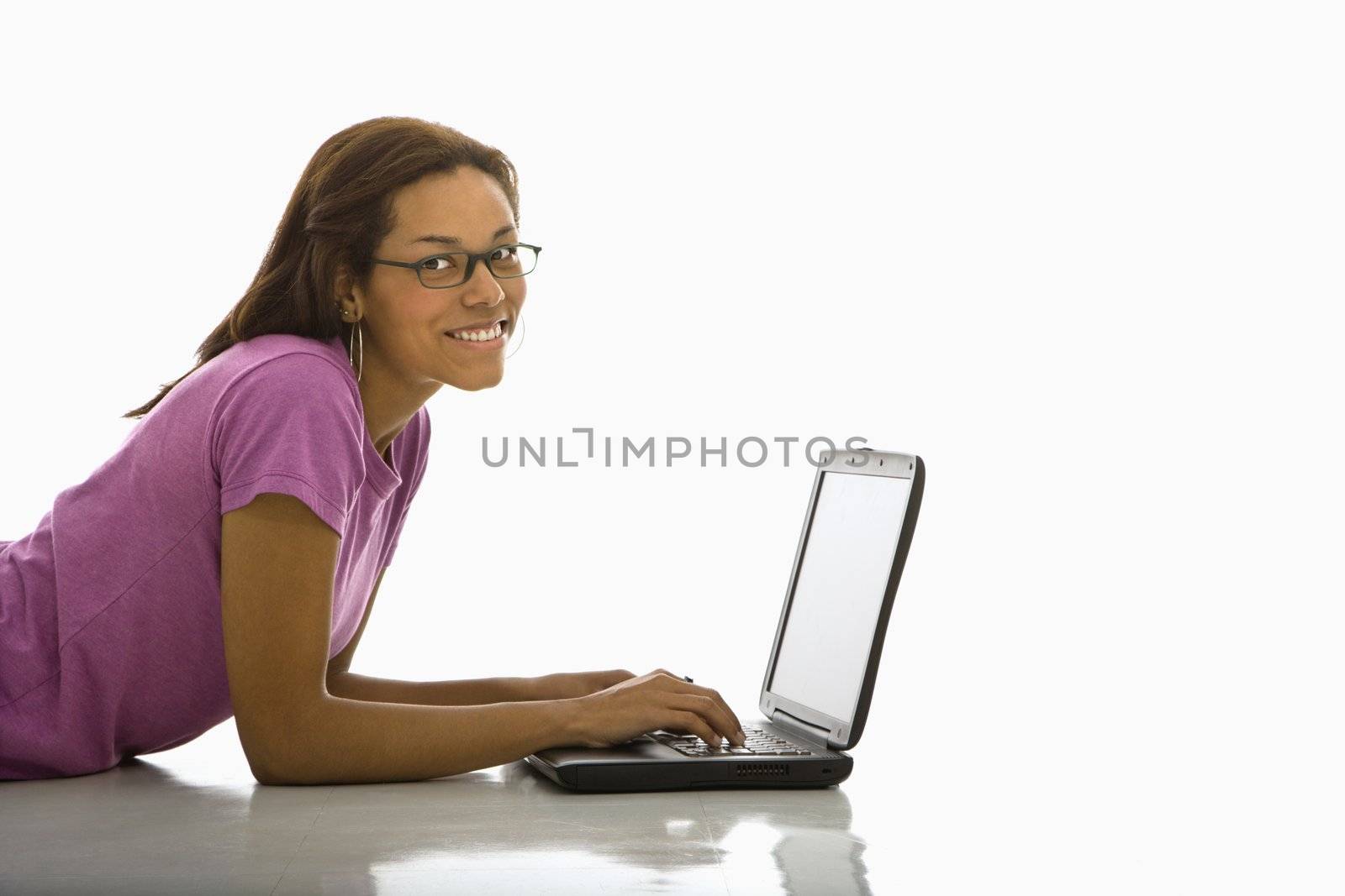 Side view of mid adult African American woman lying on floor using laptop smiling at viewer.
